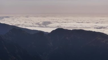 Engebeli tepeleri çevreleyen sakin sabah bulutları, sabah sisi ve uzak dağ siluetleri ile büyüleyici manzara