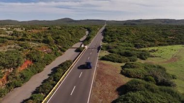 Araba yukarıda, çevresindeki canlı yeşilliklerle sessiz otoban, güneşli kırsal yol gösterişli araç ve açık gökyüzü.