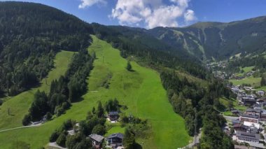 Uçan yeşil kayak yamacı çayır manzarasına dönüştü, köye doğru çimenli bir koşu, dağınık ağaçlar ve kiremitler, canlı yeşil, yaz