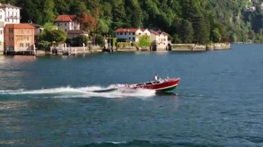 Kırmızı sürat teknesi göl kenarındaki villaları yarışıyor, kaptan köpüklü mavi sularda yüzüyor, beyaz dalgalar marinaya doğru ilerliyor.,