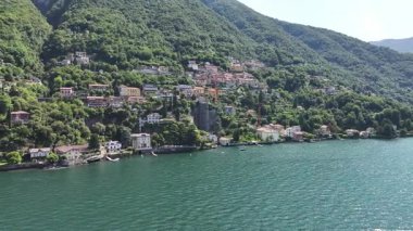 geniş göl kenarı köyü, zümrüt suyu ve yuvarlanan tepeler, küçük liman, dağınık evler ve sakin kıyı şeridi.