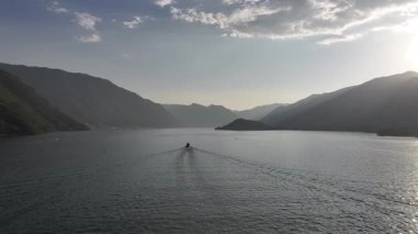 Güneş doğarken sakin göl boyunca dağ ufkuna doğru ilerleyen yalnız bir tekne uzun bir uyanış ve yumuşak altın ışık derin düşüncelere daldırır.