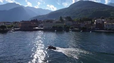 Liman yanaşma botu parıldayan suları kesiyor, güneş dalgaların üzerinde parlıyor, pastel kasaba, dağ manzarası, sinematik