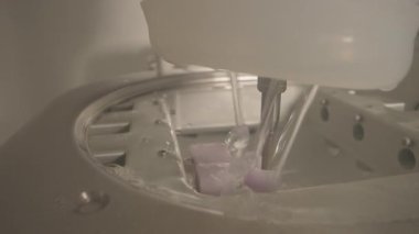 Kapalı soğutucu, değirmen odasının içindeki diş bloğundan akıyor. Mor blok hortumla durulanıyor. Metal tepside damlacıklar oluşuyor.,