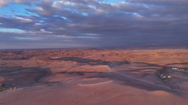 Uzak çöl yerleşim yerleri ve kum tepeleri üzerinde alacakaranlık antenleri, kıvrımlı yollar, küçük yapılar, sıcak alacakaranlık renkleri geniş.