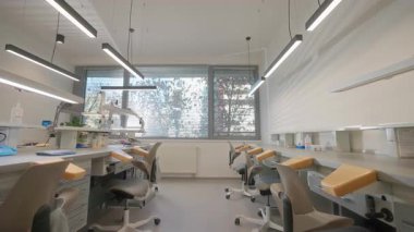 Gündüz çalışan modern diş teknisyeni, sıra sıra ergonomik sandalyeler ve tabureler, duvara monte edilmiş LED ışıklar, dağıtım üniteleri ve vakum.