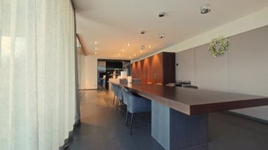 Yüksek tabureli ve katıksız perdeli uzun yemek masası, geniş tezgah, kolye ışıkları, cilalı yüzey ve açılış planı