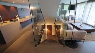 Yumuşak ışıklandırma ve pelüş kanepe ile rahat yaşam alanına inen cam merdiven, LED adım aydınlatma ve sıcak ahşap bitirir,