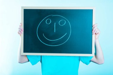 Yüzünün önünde tahtası olan, gülümseyen yüz pozitifliği olan küçük bir çocuk.