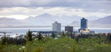 REYKJAVIK, ICELAND - 4 Haziran 2021: Reykjavik şehir merkezindeki yüksek binalar ve kışın arka planda karla kaplı dağlar.