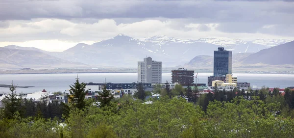 REYKJAVIK, ICELAND - JUNE 4, 2021 : Aerial view over of Reykjavik downtown with tall buildings and snow-covered mountains in background in winter time.