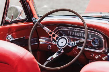 Close up shot of steering wheel and interior view of a red vintage muscle car.