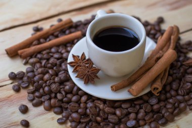 Tarçın çubuklu bir fincan kahve ve ahşap bir masada fasulye..