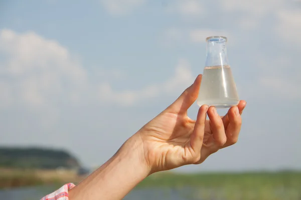 Su saflık testi su, göl veya nehir içinde belgili tanımlık geçmiş ile kimyasal bir şişesi tutan el.