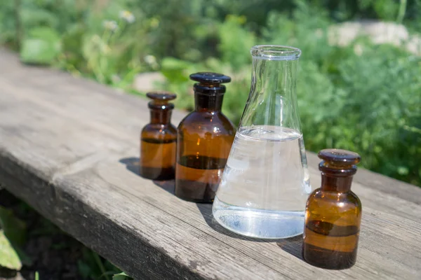 Vloeistof in chemische ware op een achtergrond van planten, meststoffen en pesticiden in de tuin. — Stockfoto