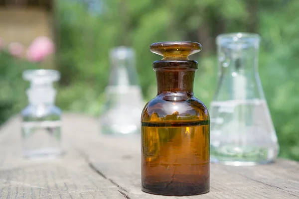 Flüssigkeit in chemischem Geschirr auf dem Hintergrund von Pflanzen, Düngemitteln oder Pestiziden im Garten. — Stockfoto