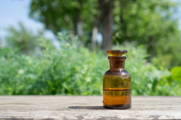 Kleine bruine fles met water of vloeistof op houten plank, tegen de achtergrond van de vegetatie. — Stockfoto