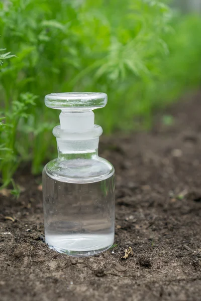 Vloeistof in chemische ware op een achtergrond van planten, meststoffen en pesticiden in de tuin. — Stockfoto