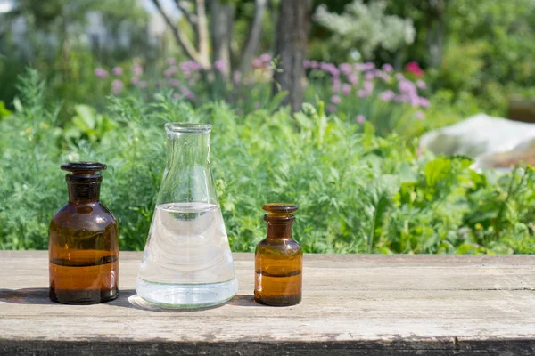 Vloeistof in chemische ware op een achtergrond van planten, meststoffen en pesticiden in de tuin. — Stockfoto