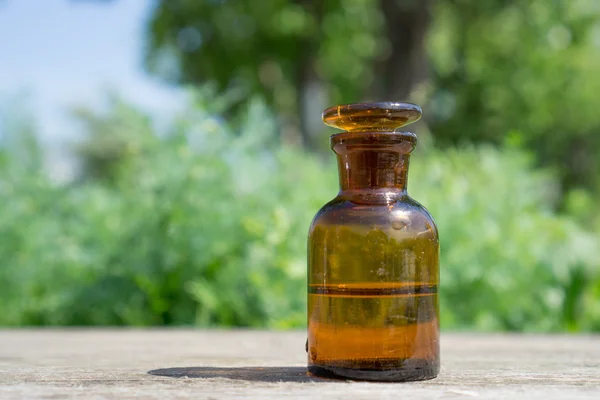 Petite bouteille brune avec eau ou liquide sur planche de bois, sur fond de végétation . — Photo