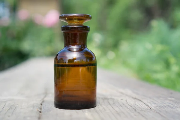 Liten brun flaska med vatten eller vätska på träplatta, mot bakgrund av vegetation. — Stockfoto