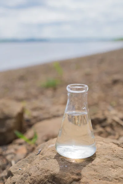 Frasco químico con agua, lago o río en el fondo . — Foto de Stock