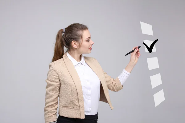 Junge Geschäftsfrau beim Ankreuzen der Checkliste. grauer Hintergrund. — Stockfoto