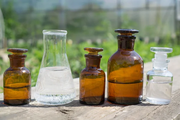 Flüssigkeit in chemischem Geschirr auf dem Hintergrund von Pflanzen, Düngemitteln oder Pestiziden im Garten. — Stockfoto