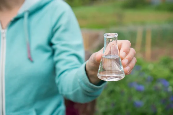 Mano con un tubo de ensayo y una planta. Fertilizante en cristalería de laboratorio . —  Fotos de Stock