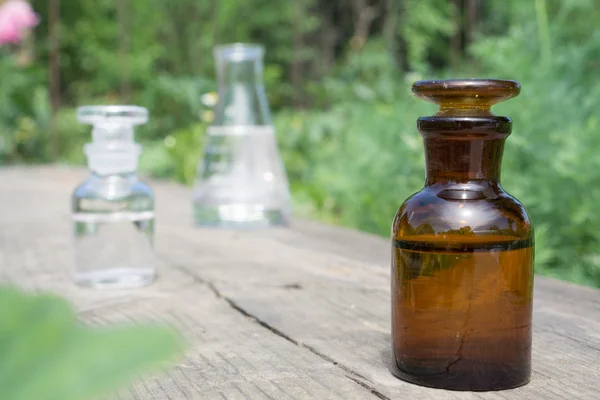 Flüssigkeit in chemischem Geschirr auf dem Hintergrund von Pflanzen, Düngemitteln oder Pestiziden im Garten. — Stockfoto