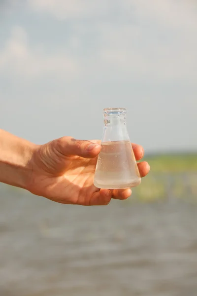 水纯度测试手拿着化学瓶与液体、 湖泊或河流中背景. — 图库照片