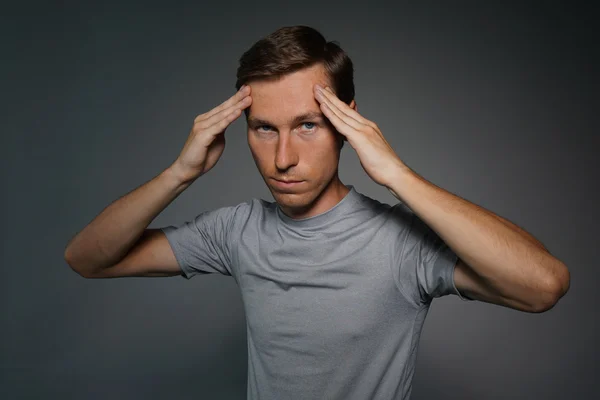 Junger Mann im T-Shirt denkt nach oder hat Kopfschmerzen. — Stockfoto