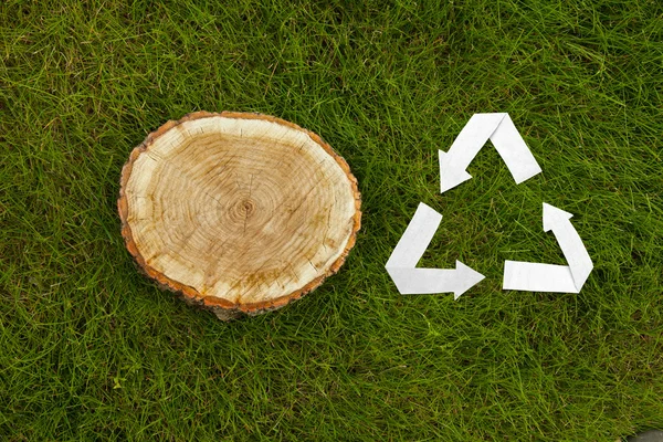 Wooden cut on grass and recycle symbol — Stock Photo, Image