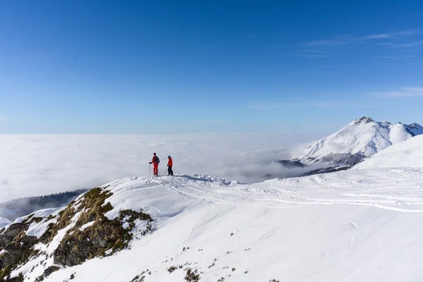 Dos esquiadores en la cima de la montaña sobre las nubes —  Fotos de Stock