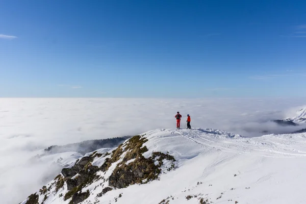 Bulutların üstünde dağın tepesinde iki kayakçı — Stok fotoğraf