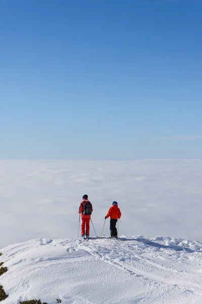 Dos esquiadores en la cima de la montaña sobre las nubes —  Fotos de Stock