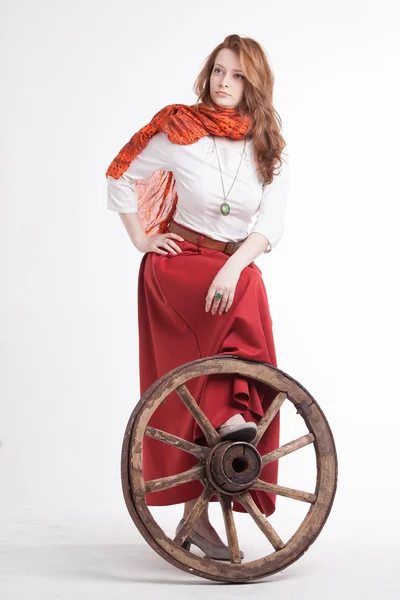 Vrouw in een lange rode rok reputatie in de buurt van wiel van de kar — Stockfoto