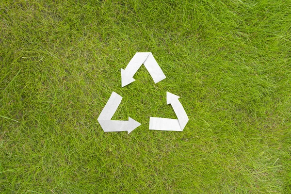 Paper recycle symbol on green grass