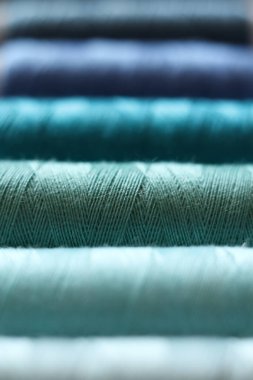 Makro yakın plan fotoğraf dikme iplik makaraları mavi ve yeşil tonlarda yumuşak bulanık ve sığ alan derinliğinde. Görüntü ince tekstil liflerini, katmanlı renkleri ve pürüzsüz dokuyu vurguluyor. Dikiş, terzi, el yapımı.