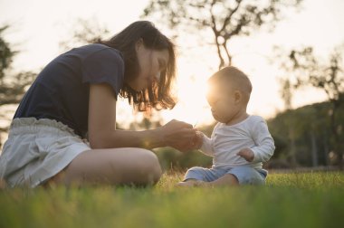 Genç Asyalı anne oğluyla mı oynuyor yoksa açık hava parkında yerde tatlı bir bebek mi?.