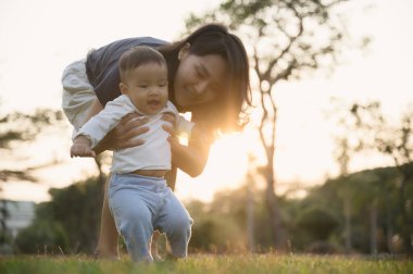 Genç Asyalı anne oğluyla mı oynuyor yoksa açık hava parkında yerde tatlı bir bebek mi?.