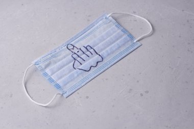 Fuck mask. A medical blue protective mask against viral infections, coronavirus lies on a modern light white concrete background.