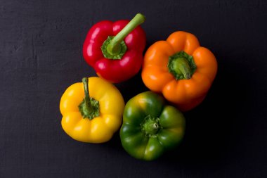 Parlak renkli dolmalık biberler siyah ve modern bir arka planda yatar. Kırmızı biber, turuncu, sarı ve yeşil dolma biber. Düz yat, üst görünüm, maket yap..