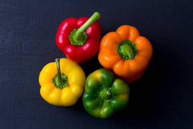 Parlak renkli dolmalık biberler siyah ve modern bir arka planda yatar. Kırmızı biber, turuncu, sarı ve yeşil dolma biber. Düz yat, üst görünüm, maket yap..