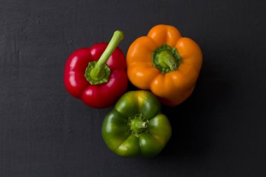 Parlak renkli dolmalık biberler siyah ve modern bir arka planda yatar. Kırmızı biber, turuncu, sarı ve yeşil dolma biber. Düz yat, üst görünüm, maket yap..