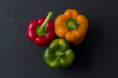 Parlak renkli dolmalık biberler siyah ve modern bir arka planda yatar. Kırmızı biber, turuncu, sarı ve yeşil dolma biber. Düz yat, üst görünüm, maket yap..