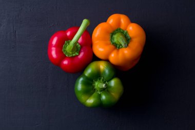 Parlak renkli dolmalık biberler siyah ve modern bir arka planda yatar. Kırmızı biber, turuncu, sarı ve yeşil dolma biber. Düz yat, üst görünüm, maket yap..