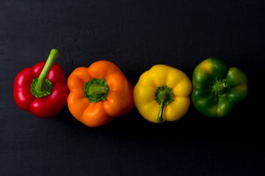 Parlak renkli dolmalık biberler siyah ve modern bir arka planda yatar. Kırmızı biber, turuncu, sarı ve yeşil dolma biber. Düz yat, üst görünüm, maket yap..