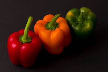 Parlak renkli dolmalık biberler siyah ve modern bir arka planda yatar. Kırmızı biber, turuncu, sarı ve yeşil dolma biber. Düz yat, üst görünüm, maket yap..