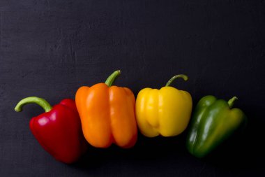 Parlak renkli dolmalık biberler siyah ve modern bir arka planda yatar. Kırmızı biber, turuncu, sarı ve yeşil dolma biber. Düz yat, üst görüş, maket yap. Boşluğu kopyala.